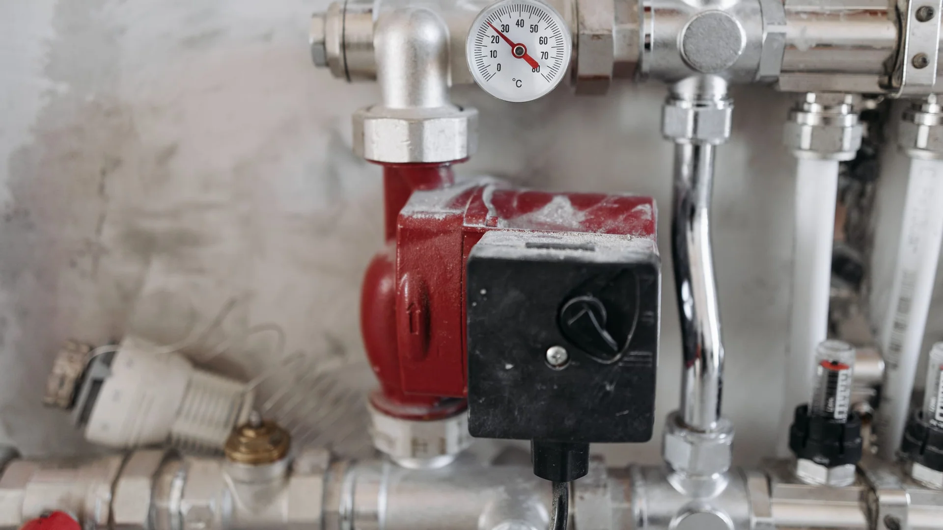 Hydronic manifold with red circulation pump and temperature gauge in a heat pump installation